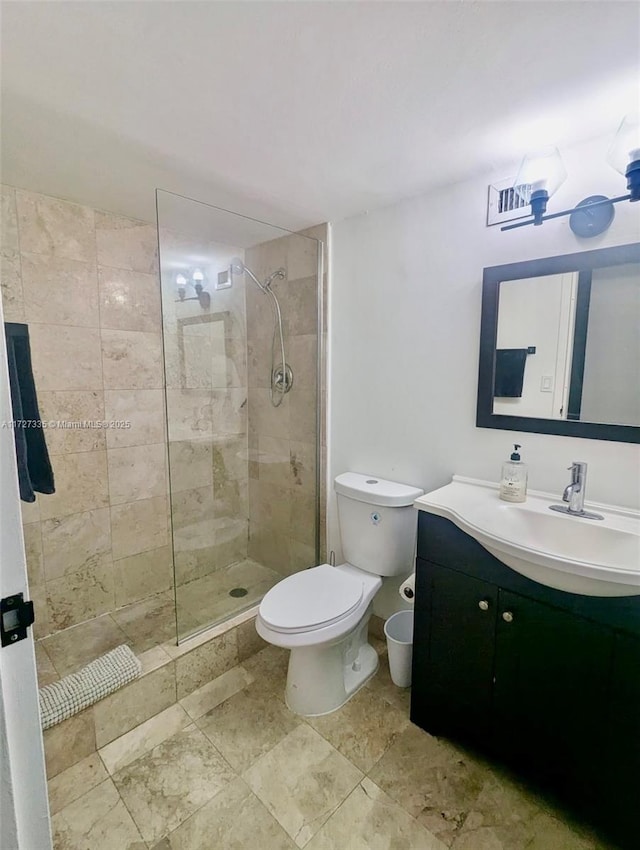 bathroom with toilet, a tile shower, and vanity