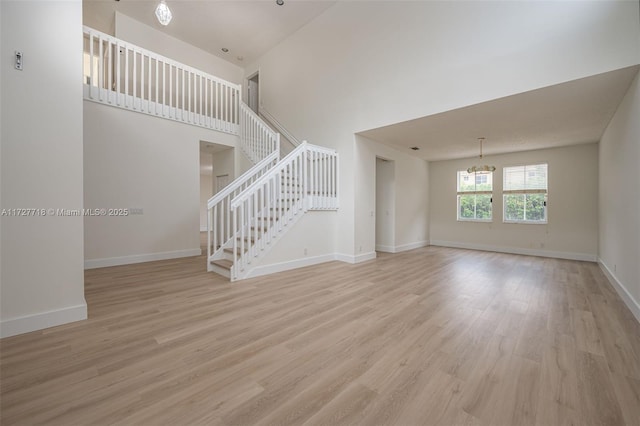 unfurnished living room with light hardwood / wood-style floors, a high ceiling, and a chandelier