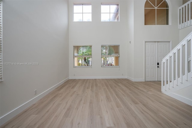 unfurnished living room featuring a towering ceiling and light hardwood / wood-style floors