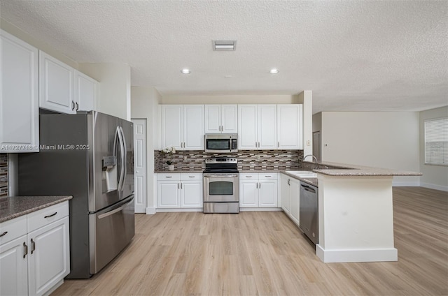 kitchen with appliances with stainless steel finishes, tasteful backsplash, white cabinets, a textured ceiling, and light hardwood / wood-style flooring