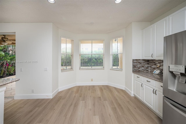 kitchen featuring light stone countertops, stainless steel refrigerator with ice dispenser, white cabinetry, decorative backsplash, and plenty of natural light