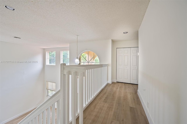 hallway with light wood-type flooring, an inviting chandelier, and a textured ceiling