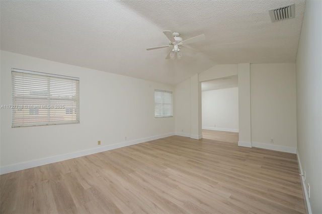 spare room with light wood-type flooring, vaulted ceiling, a textured ceiling, and ceiling fan