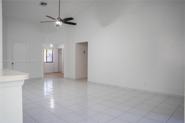 tiled empty room with ceiling fan and a high ceiling