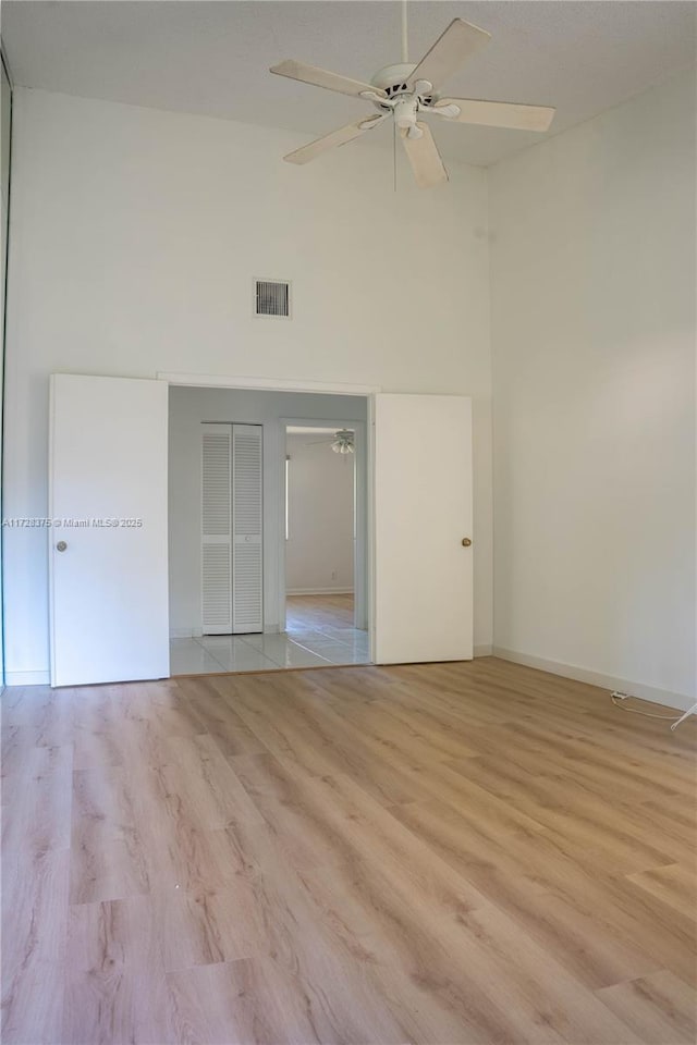 empty room featuring ceiling fan, a high ceiling, and light wood-type flooring