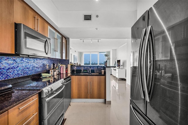 kitchen with stainless steel appliances, tasteful backsplash, dark stone countertops, sink, and light tile patterned flooring