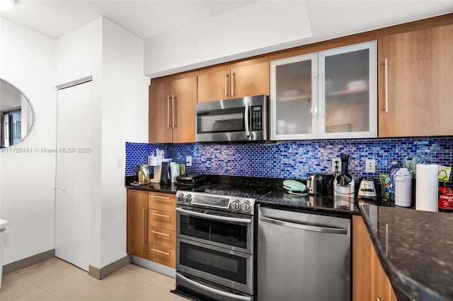 kitchen with light tile patterned flooring, appliances with stainless steel finishes, decorative backsplash, and dark stone countertops