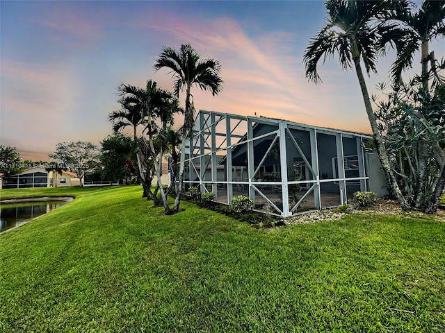 yard at dusk featuring a lanai and a water view