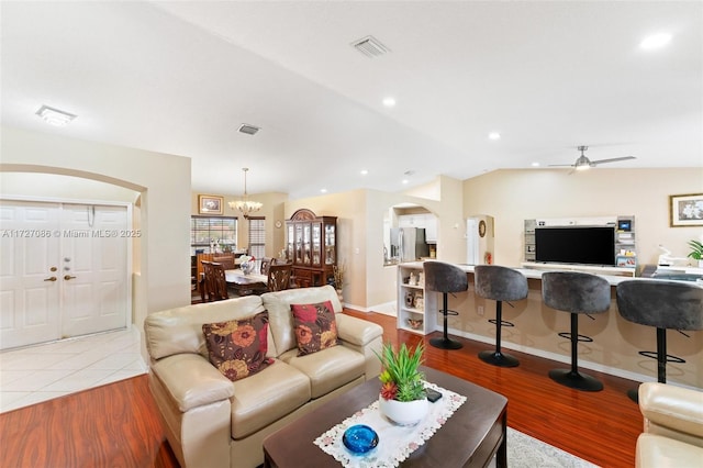 living room with ceiling fan with notable chandelier, vaulted ceiling, and light wood-type flooring