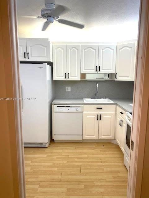 kitchen featuring ceiling fan, sink, white appliances, light wood-type flooring, and white cabinets