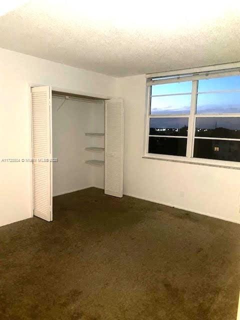 unfurnished bedroom with a textured ceiling, a closet, and dark colored carpet