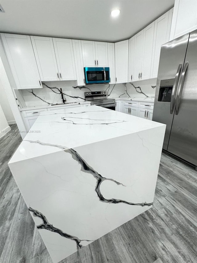 kitchen featuring light stone countertops, appliances with stainless steel finishes, white cabinetry, tasteful backsplash, and light hardwood / wood-style flooring