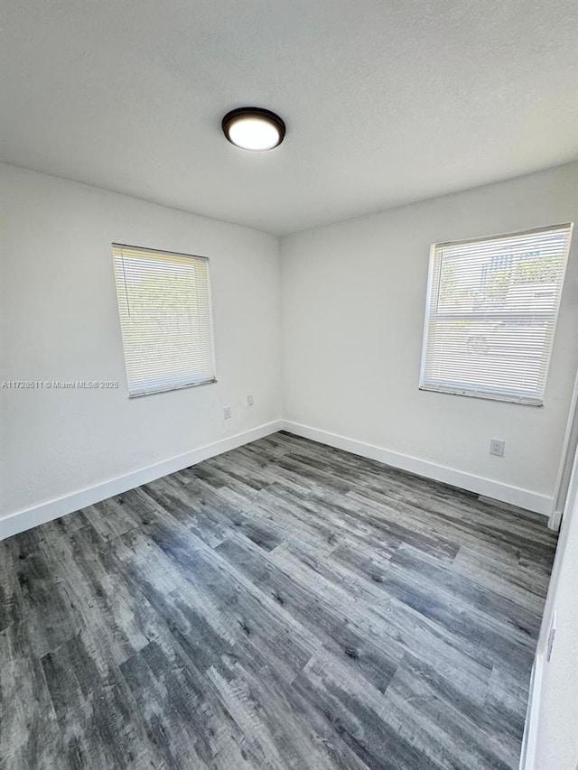 empty room with a textured ceiling, a healthy amount of sunlight, and dark hardwood / wood-style floors