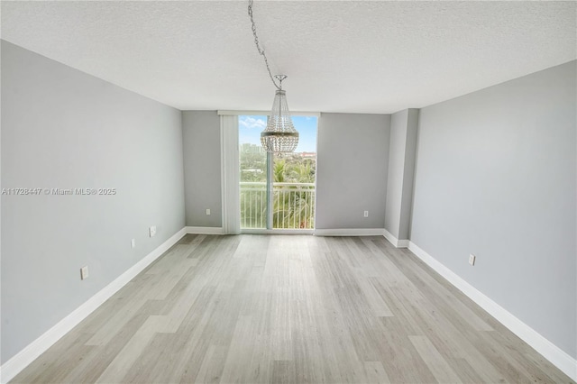 empty room featuring a textured ceiling, a wall of windows, light hardwood / wood-style flooring, and a chandelier