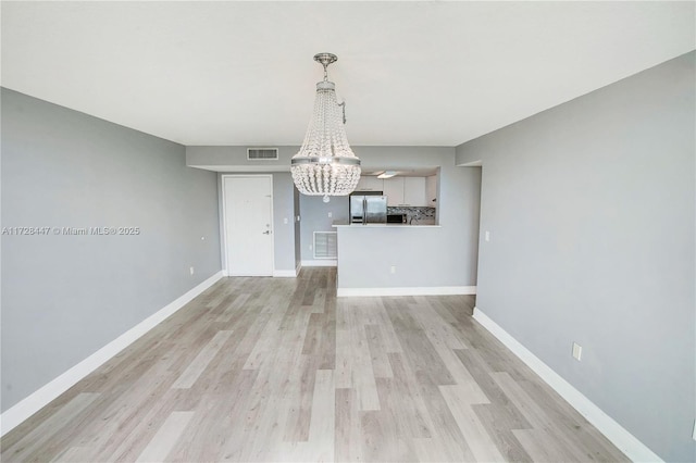 unfurnished dining area featuring an inviting chandelier and light hardwood / wood-style flooring