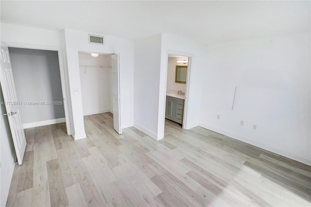 unfurnished bedroom featuring ensuite bath, a walk in closet, a closet, and light hardwood / wood-style flooring