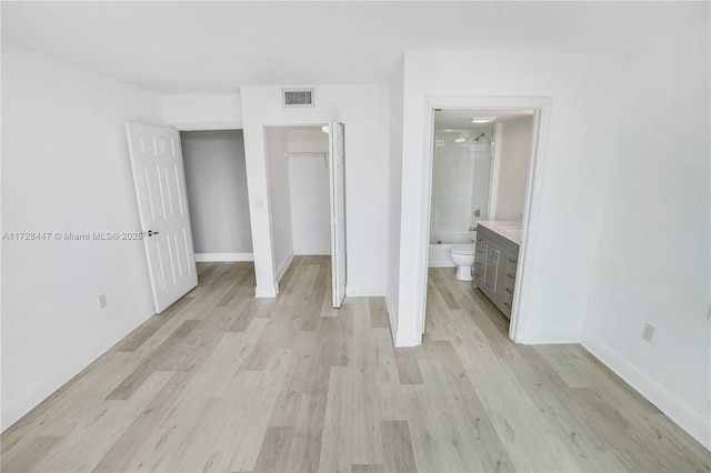 unfurnished bedroom with a closet, ensuite bath, and light wood-type flooring