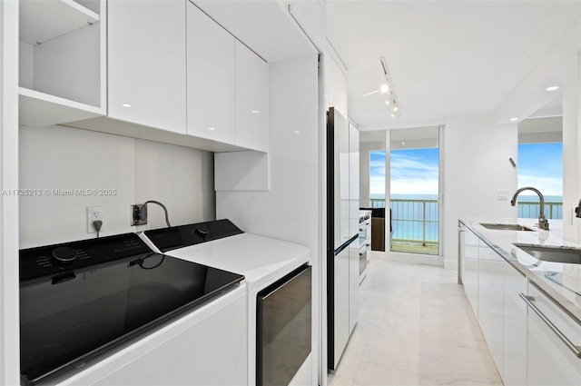 clothes washing area featuring separate washer and dryer, rail lighting, a water view, and sink