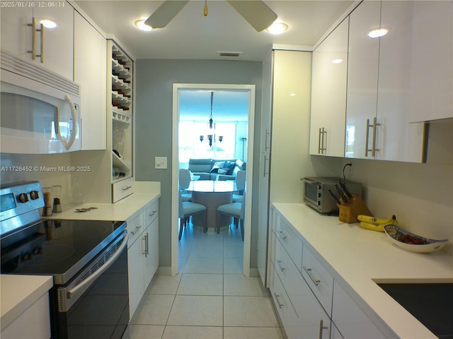 kitchen featuring light tile patterned flooring, hanging light fixtures, electric stove, ceiling fan, and white cabinets