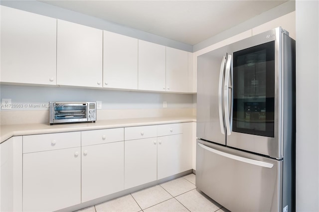 kitchen with stainless steel refrigerator, white cabinetry, and light tile patterned floors