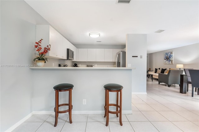 kitchen with stainless steel appliances, kitchen peninsula, white cabinets, and a kitchen bar