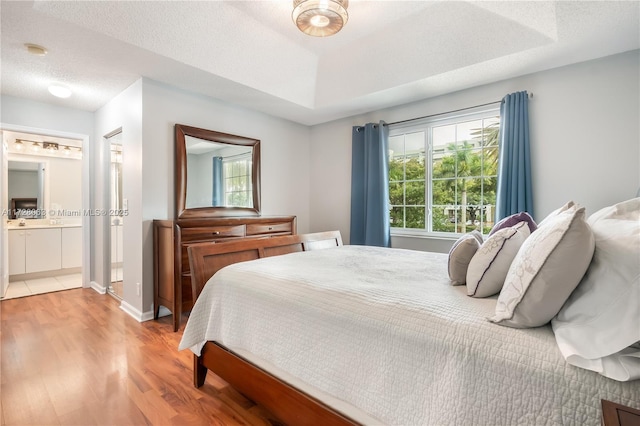 bedroom featuring ensuite bathroom, light hardwood / wood-style flooring, a textured ceiling, and a tray ceiling