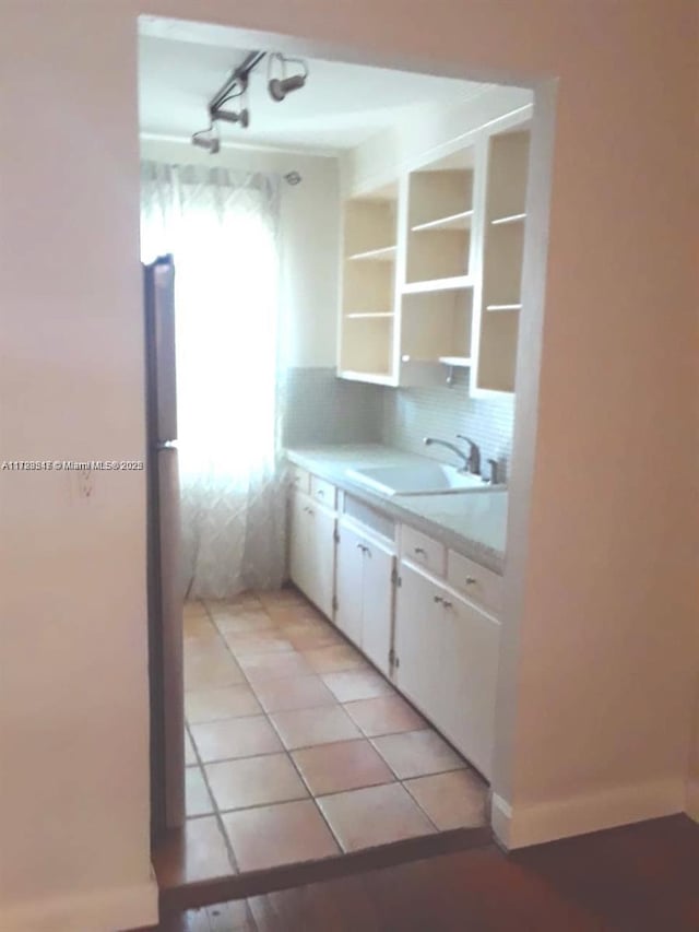 kitchen featuring light tile patterned floors, sink, backsplash, and white cabinets