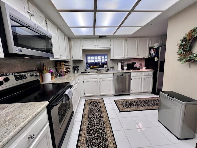 kitchen featuring decorative backsplash, sink, light tile patterned floors, stainless steel appliances, and white cabinets