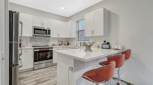 kitchen featuring kitchen peninsula, a breakfast bar area, stainless steel appliances, white cabinets, and light hardwood / wood-style flooring