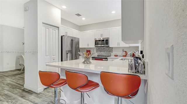 kitchen with a kitchen bar, kitchen peninsula, stainless steel appliances, white cabinets, and sink