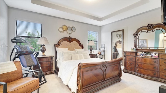 bedroom featuring light carpet, a tray ceiling, and multiple windows