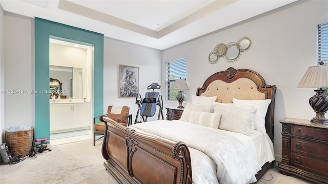 bedroom with ensuite bath, light colored carpet, and a tray ceiling