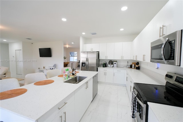 kitchen featuring sink, appliances with stainless steel finishes, white cabinetry, a center island, and light stone counters