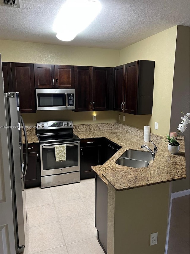 kitchen featuring dark brown cabinetry, appliances with stainless steel finishes, sink, kitchen peninsula, and light stone counters