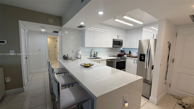 kitchen featuring kitchen peninsula, sink, a kitchen breakfast bar, stainless steel appliances, and white cabinets