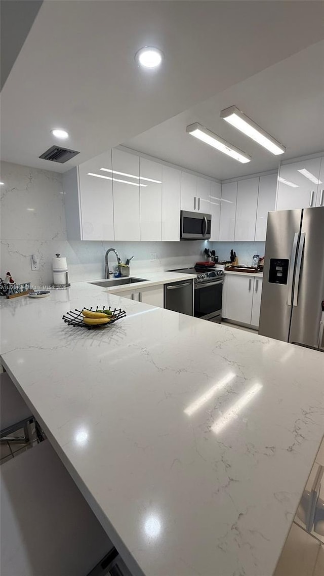 kitchen featuring white cabinetry, stainless steel appliances, sink, kitchen peninsula, and a breakfast bar area