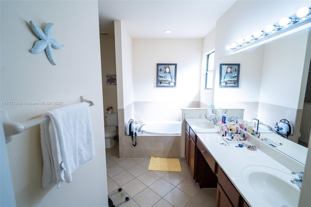 bathroom with tiled tub, vanity, tile patterned flooring, and toilet