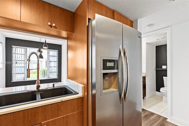 kitchen with stainless steel fridge, a textured ceiling, pendant lighting, light hardwood / wood-style flooring, and sink