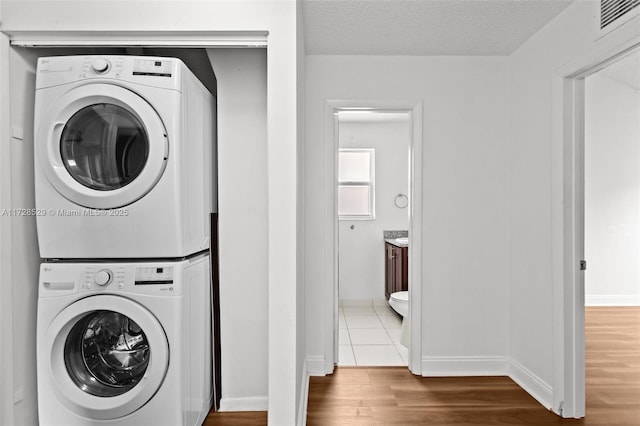 clothes washing area featuring stacked washer / dryer, a textured ceiling, and tile patterned flooring