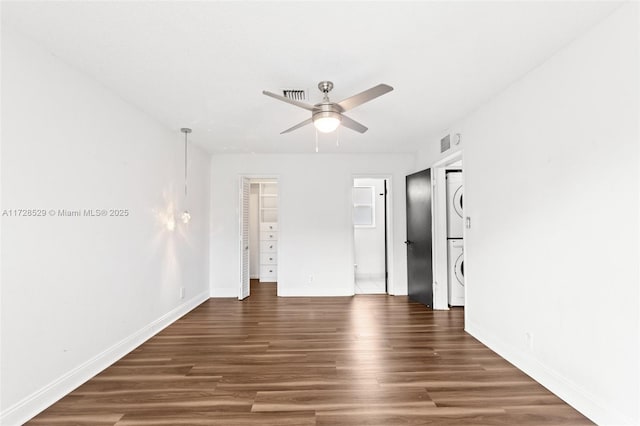 empty room featuring ceiling fan, dark hardwood / wood-style flooring, and stacked washer and clothes dryer