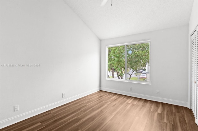 unfurnished room featuring a textured ceiling, light hardwood / wood-style flooring, and vaulted ceiling