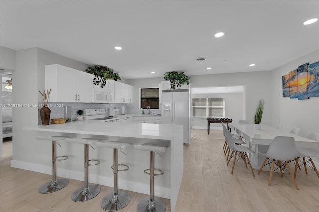 kitchen with white cabinetry, kitchen peninsula, white appliances, a breakfast bar, and sink