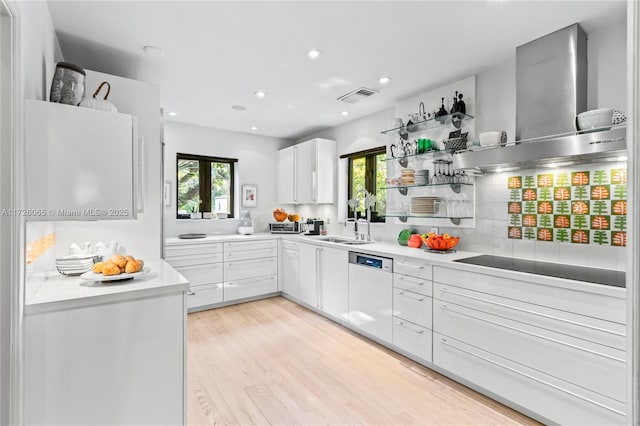 kitchen featuring white cabinetry, light hardwood / wood-style floors, white dishwasher, wall chimney range hood, and sink