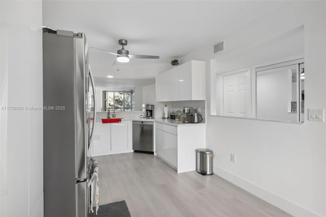 kitchen with white cabinets, stainless steel appliances, kitchen peninsula, ceiling fan, and light hardwood / wood-style flooring