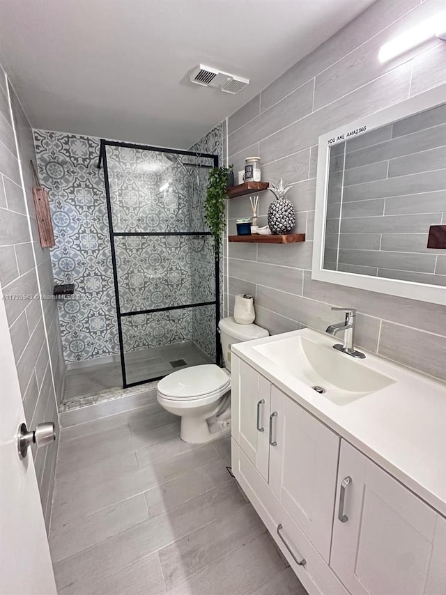 bathroom with toilet, tiled shower, tile patterned flooring, tile walls, and vanity