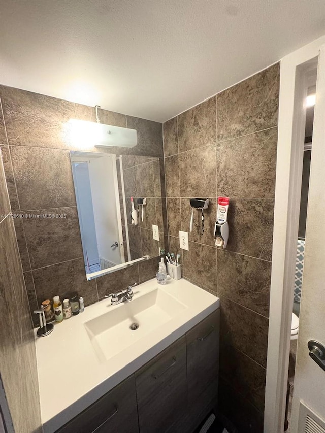 bathroom featuring toilet, decorative backsplash, tile walls, and vanity