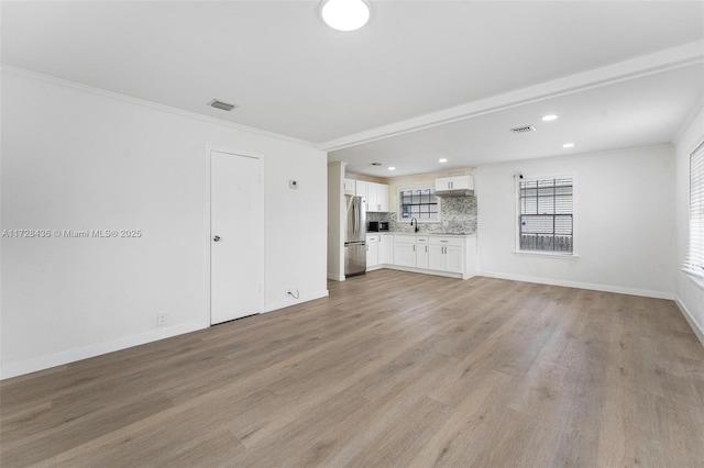 unfurnished living room with sink, ornamental molding, and light hardwood / wood-style floors