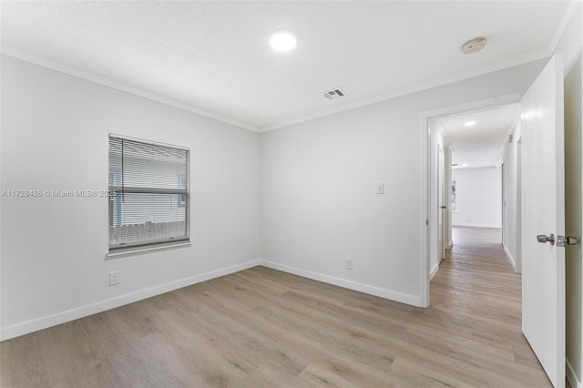 spare room with crown molding, light wood finished floors, baseboards, and visible vents