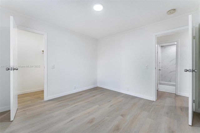 unfurnished bedroom with baseboards, a spacious closet, and light wood-type flooring