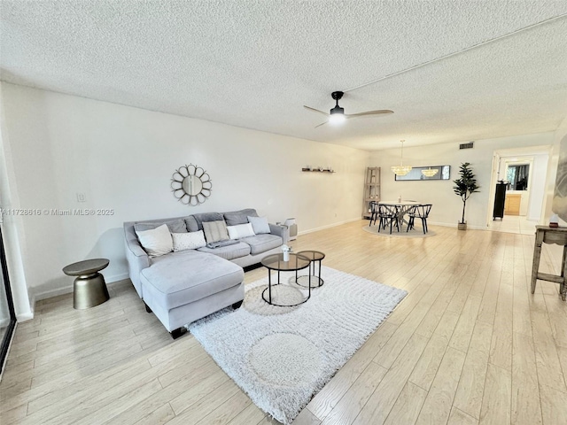 living room with ceiling fan, a textured ceiling, and light hardwood / wood-style floors